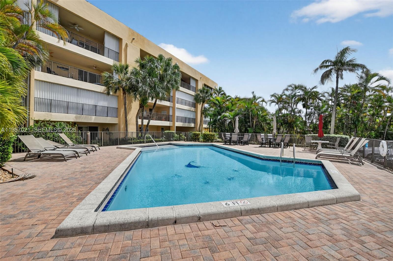 An outdoor swimming pool is surrounded by a brick patio and lounge chairs near apartments — 333 SE 20th Ave, Deerfield Beach FL 33441, DEERFIELD BEACH, FL