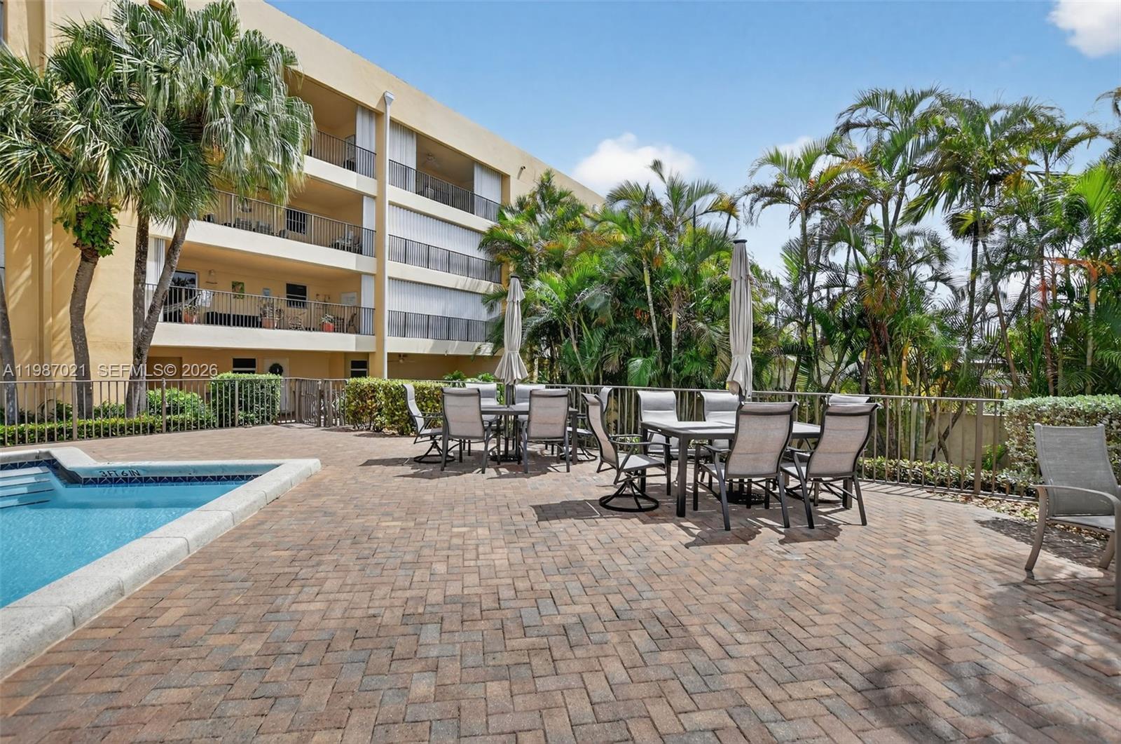 A paved pool deck features outdoor dining sets and palm trees beside a multi-story building — 333 SE 20th Ave, Deerfield Beach FL 33441, DEERFIELD BEACH, FL