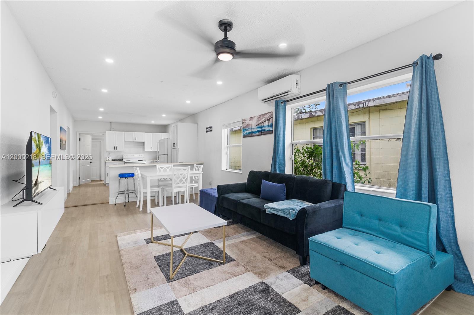A living room and kitchen area features light wood flooring, a dark sofa, and blue curtains — 1408 N 23rd St # 0, Fort Pierce FL 34950, FORT PIERCE, FL