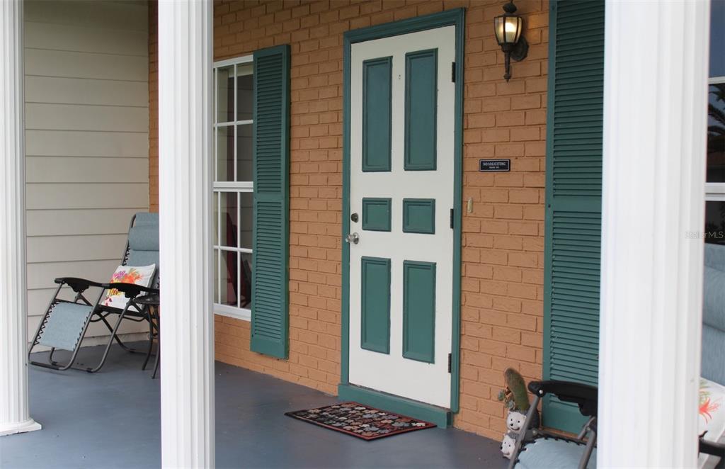 A front porch with a brick wall, a white door, and two folding chairs — 2320 ALTON ROAD, PORT CHARLOTTE, FL