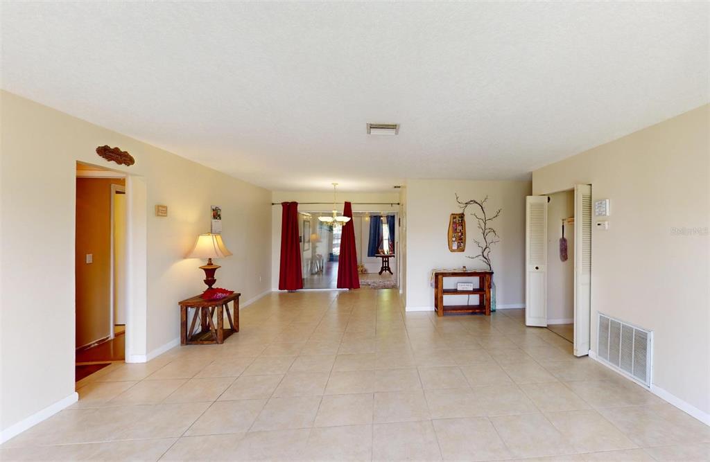 A spacious, tiled living area features beige walls, a central chandelier, and red curtains — 2320 ALTON ROAD, PORT CHARLOTTE, FL