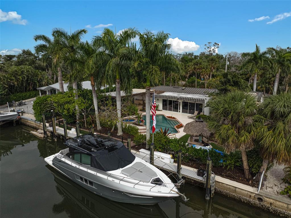 An aerial view shows a waterfront house with a pool, palm trees, and a docked boat — 4508 WOODSIDE ROAD, SARASOTA, FL