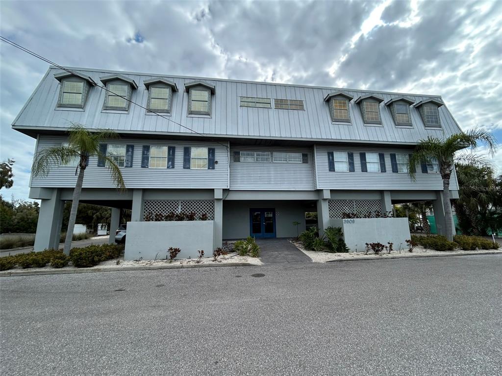 A three-story building with a metal roof, gray siding, and an elevated ground level — 3909 E BAY DRIVE UNIT 4, HOLMES BEACH, FL