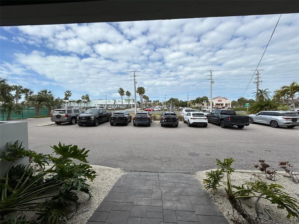 A paved walkway leads to a parking lot filled with various vehicles under a cloudy sky — 3909 E BAY DRIVE UNIT 4, HOLMES BEACH, FL