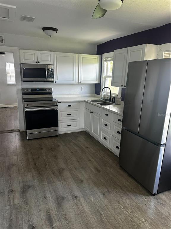 A kitchen features white cabinets, stainless steel appliances, a dark accent wall, and wood-look flooring — 4411 16TH AVENUE S, ST PETERSBURG, FL