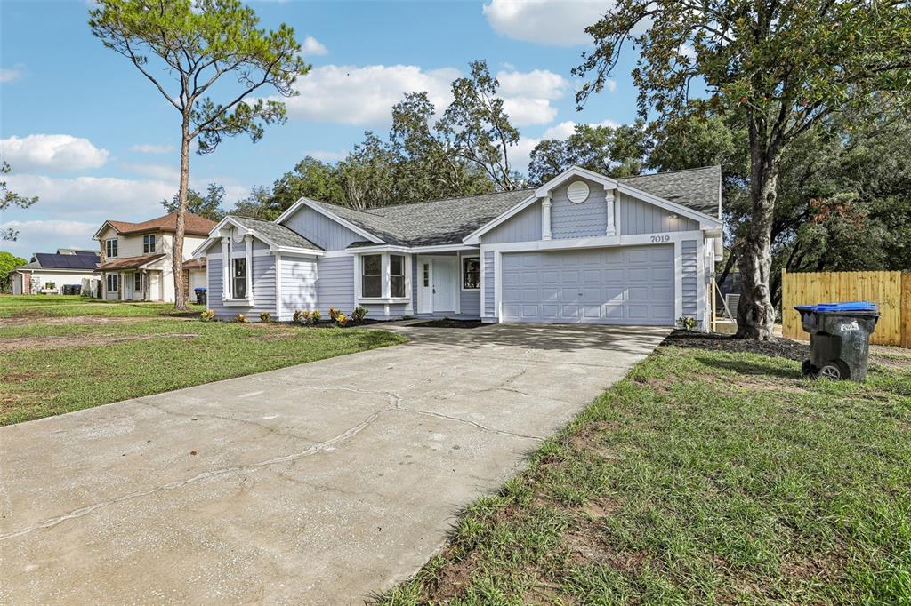 A light blue single-story house with a concrete driveway and a two-car garage — 7019 KENSINGTON HIGH BOULEVARD, ORLANDO, FL