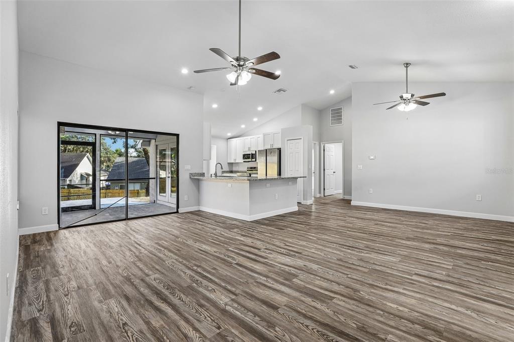 An open-concept living area features wood-look flooring, a kitchen with white cabinets, and sliding glass doors — 7019 KENSINGTON HIGH BOULEVARD, ORLANDO, FL