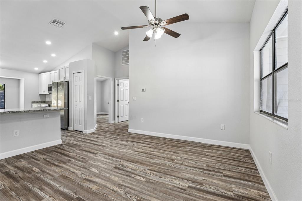 A bright, open-concept living area features wood-look flooring, a ceiling fan, and an adjacent kitchen — 7019 KENSINGTON HIGH BOULEVARD, ORLANDO, FL