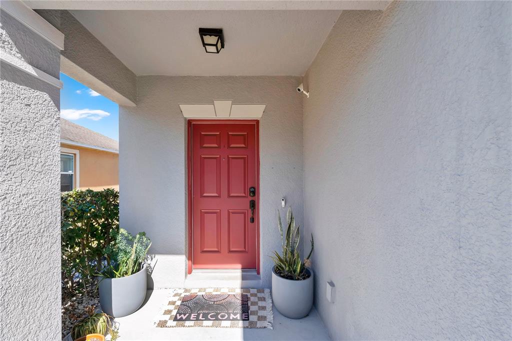 A red front door sits under a covered entryway with two potted plants and a mat — 643 WASHINGTON WAY, HAINES CITY, FL