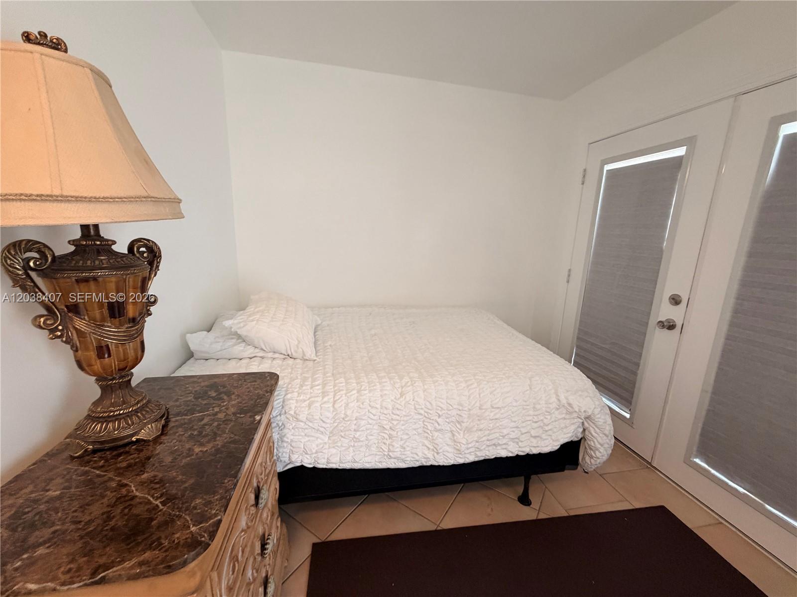 A bedroom features a bed, a lamp on a marble-topped dresser, and glass doors — 5931 SW 148th Pl # 1, Miami FL 33193, MIAMI, FL