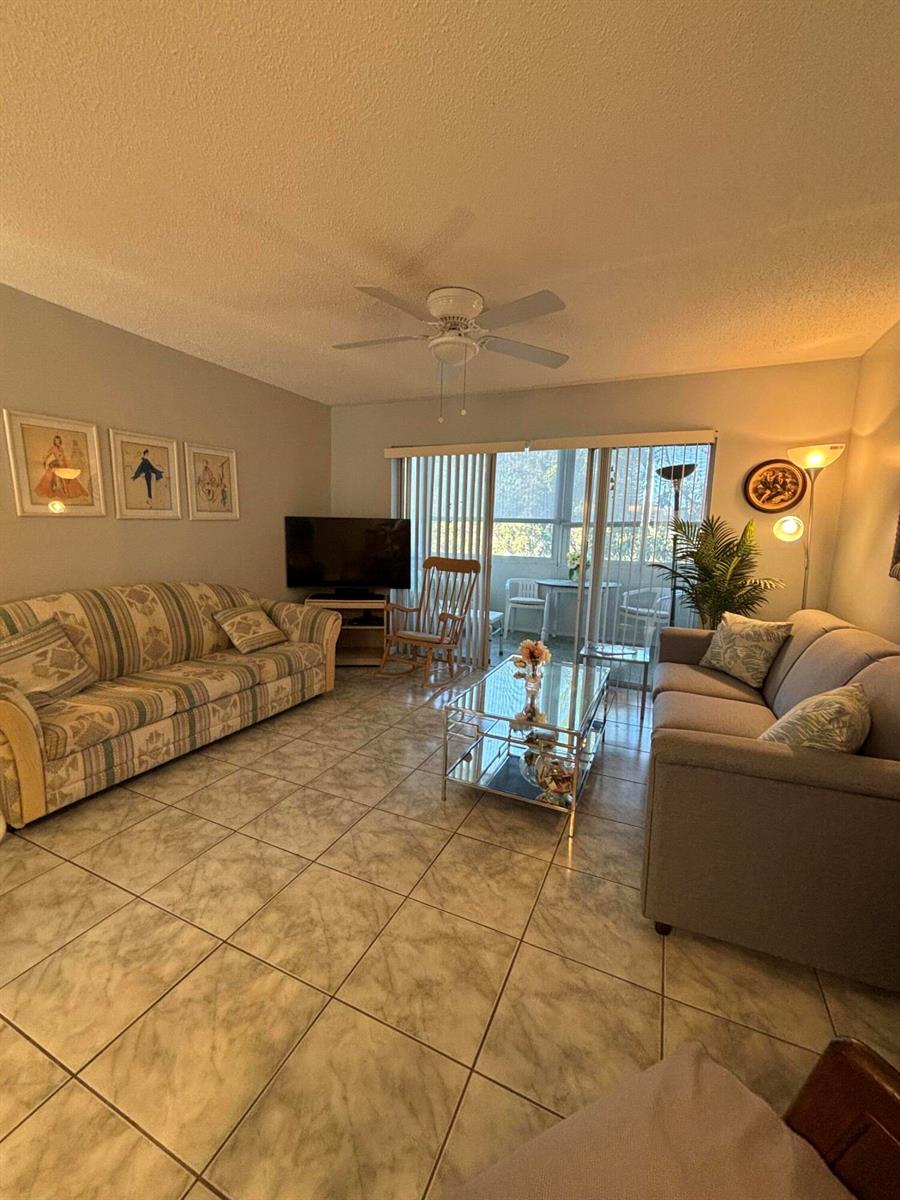 A living room features tile flooring, two sofas, a glass coffee table, and a sliding door — 725 Lori Drive # 203, Palm Springs FL 33461, PALM SPRINGS, FL