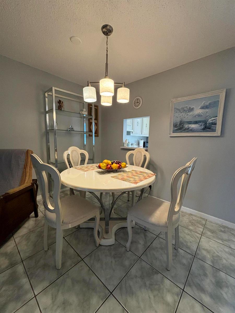 A dining room features a round white table, four chairs, and a modern light fixture — 725 Lori Drive # 203, Palm Springs FL 33461, PALM SPRINGS, FL