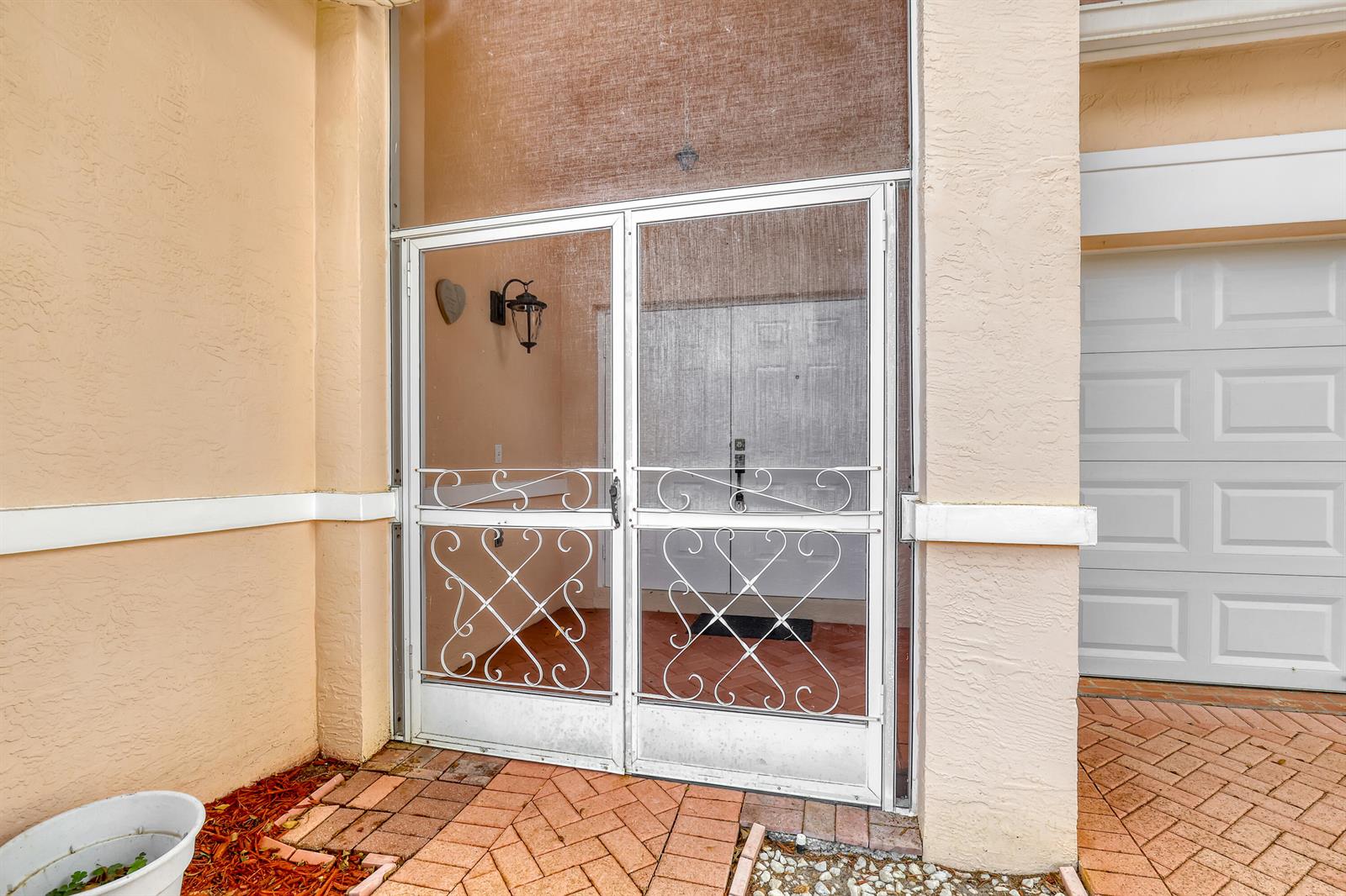 A white metal screen door stands at the entrance of a home with brick pavers — 180 Caribe Court, FL 33413, FL
