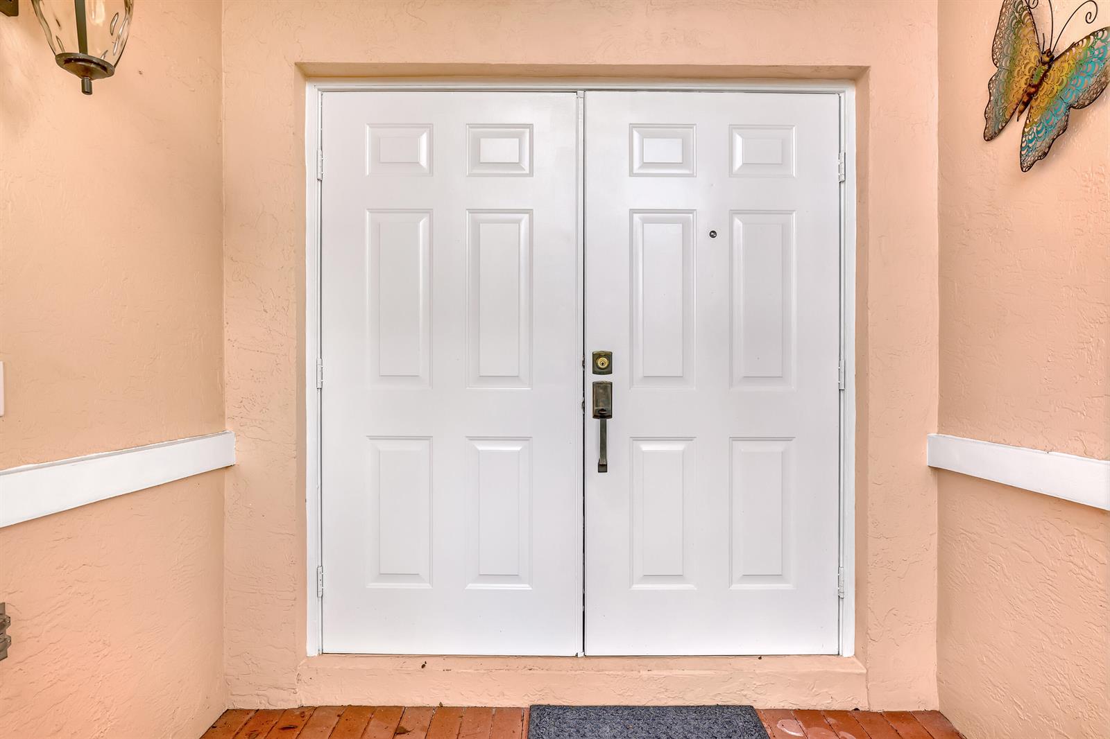 A white double front door with six panels is set into a peach-colored exterior wall — 180 Caribe Court, FL 33413, FL