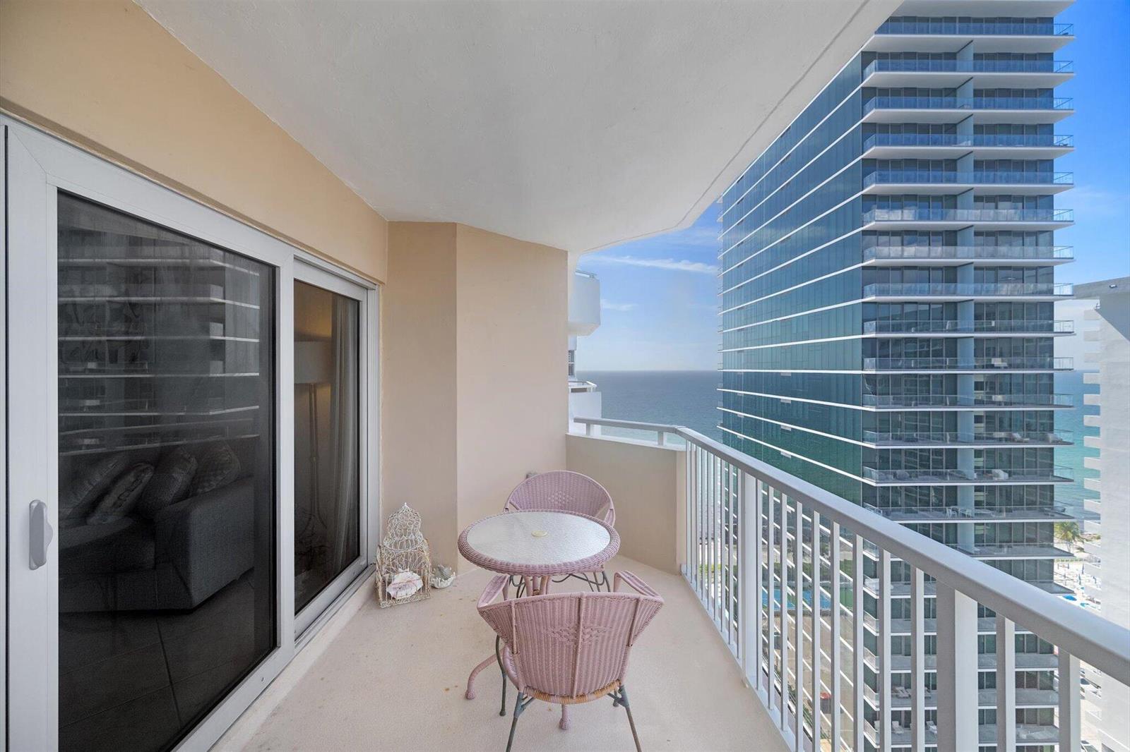 A balcony with a small table and two chairs overlooks the ocean and a skyscraper — 1980 S Ocean Drive # 19a, Hallandale Beach FL 33009, HALLANDALE BEACH, FL