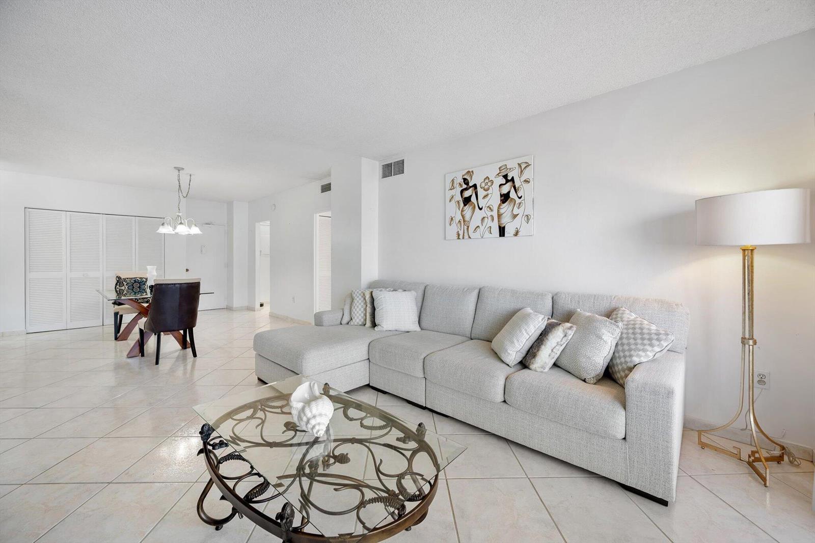 A living room with a light gray sectional sofa, glass coffee table, and tile flooring — 1980 S Ocean Drive # 19a, Hallandale Beach FL 33009, HALLANDALE BEACH, FL