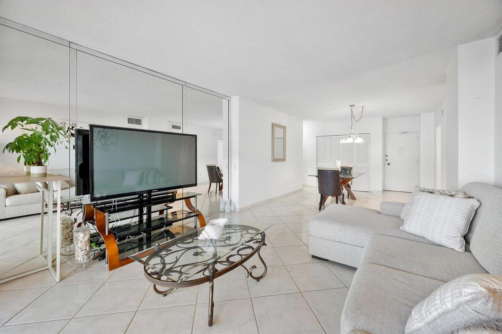 A living room with tile floors, a mirrored wall, a television, and a sectional sofa — 1980 S Ocean Drive # 19a, Hallandale Beach FL 33009, HALLANDALE BEACH, FL