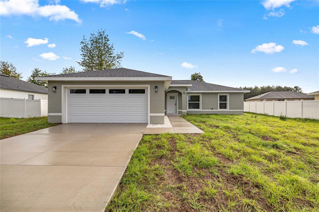 A single-story house with a two-car garage, gray stucco exterior, and a white fence — 181 PINE COURSE, OCALA, FL