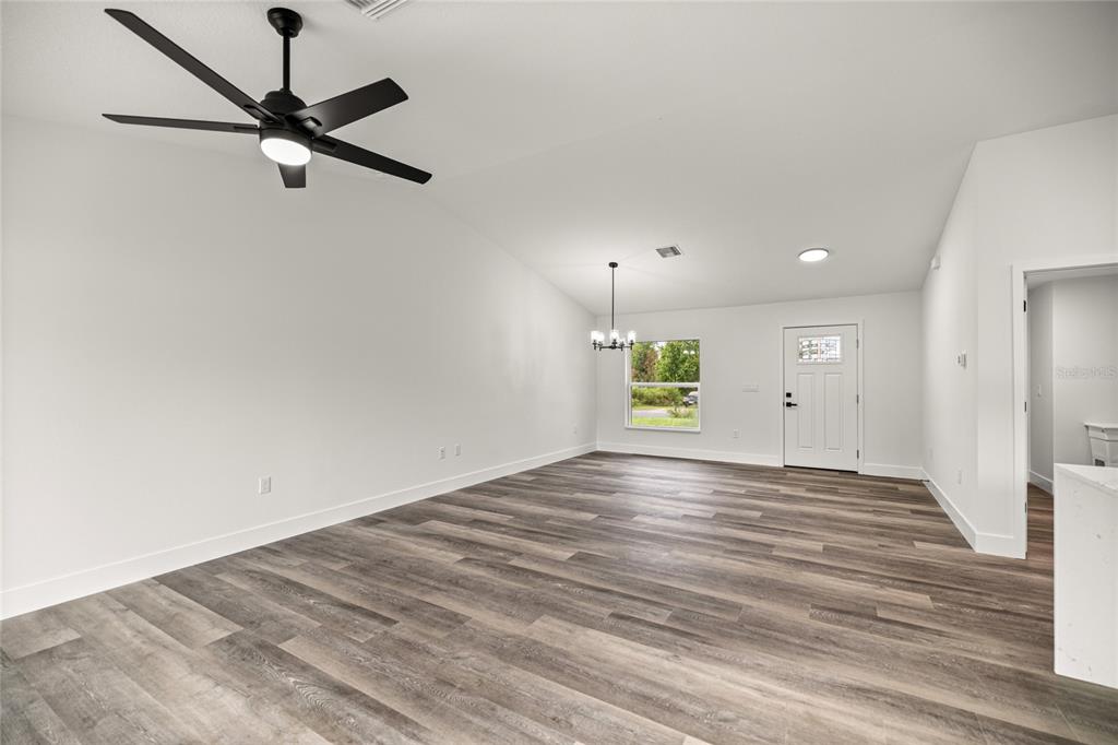An open-concept living and dining area features wood-look flooring, a vaulted ceiling, and a ceiling fan — 181 PINE COURSE, OCALA, FL