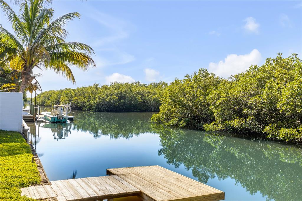 A wooden dock extends into a canal lined with mangroves and a small boat — 4602 SAXON DRIVE, NEW SMYRNA BEACH, FL