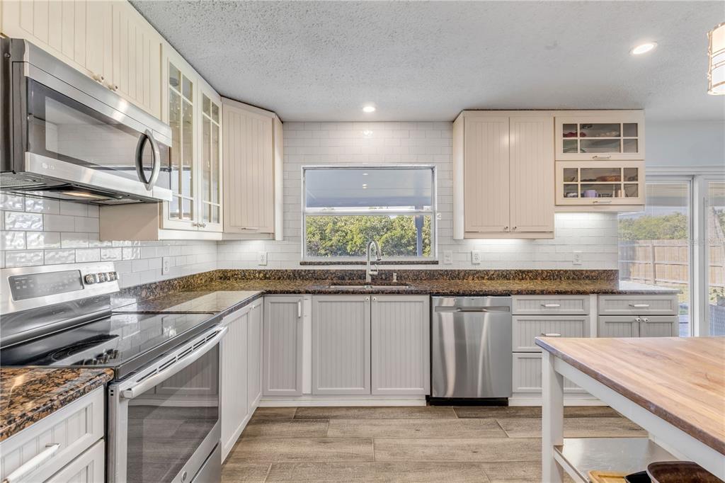 A kitchen with light-colored cabinets, stainless steel appliances, granite countertops, and a subway tile backsplash — 4602 SAXON DRIVE, NEW SMYRNA BEACH, FL