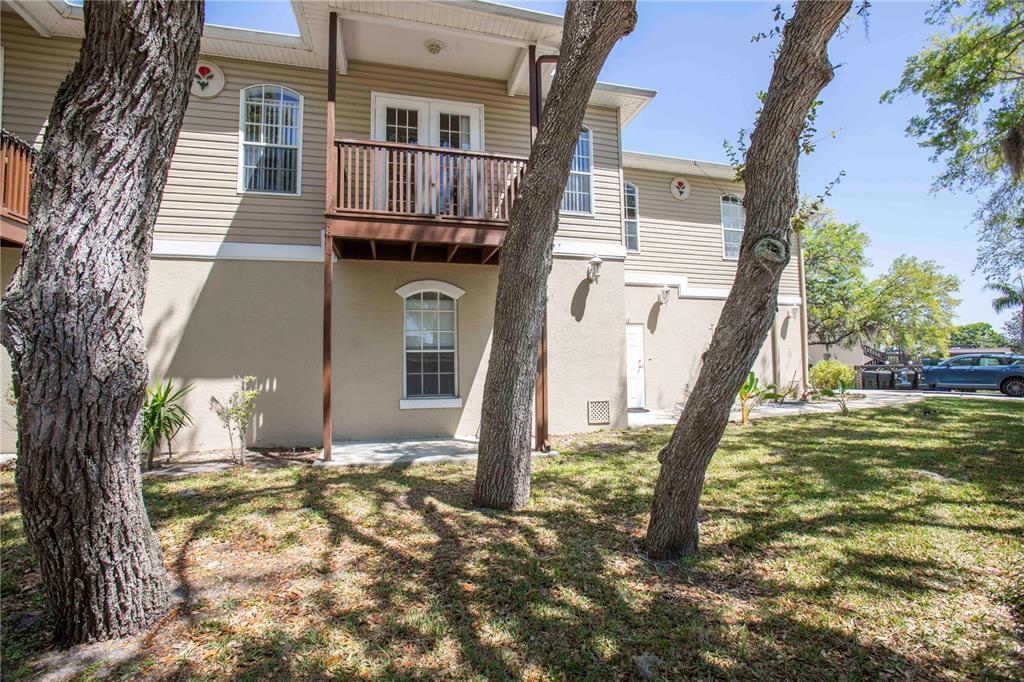 The exterior of a two-story apartment building features beige siding, a wooden balcony, and trees — 4751 W MARINE PARKWAY UNIT 4751, NEW PORT RICHEY, FL