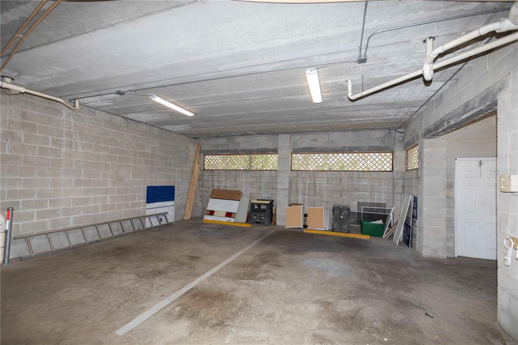 An unfinished concrete block garage with exposed pipes, fluorescent lighting, and a white entry door — 4751 W MARINE PARKWAY UNIT 4751, NEW PORT RICHEY, FL