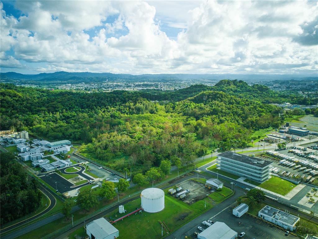 An aerial view shows a large industrial complex with a white storage tank and surrounding forest — CARRETERA 2, KM 3.1, BAYAMON, PR