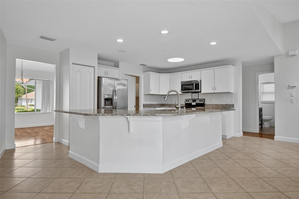 A kitchen features white cabinets, granite countertops, a central island, and light-colored tile flooring — 231 WELLINGTON DRIVE, PALM COAST, FL