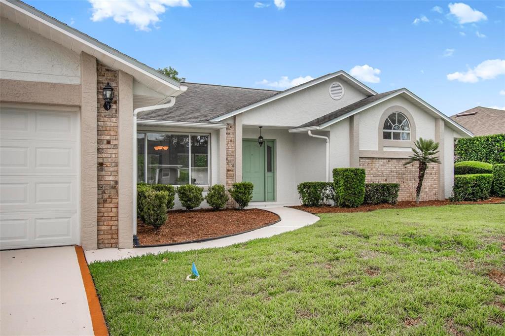 A single-story house features a light-colored exterior, a green front door, and a brick facade — 231 WELLINGTON DRIVE, PALM COAST, FL
