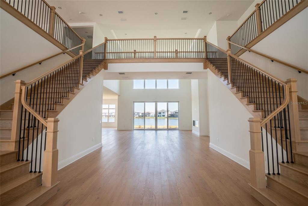 A grand foyer features dual staircases, light wood flooring, and a large window overlooking water — 9760 LAUREL BERRY DRIVE, ORLANDO, FL
