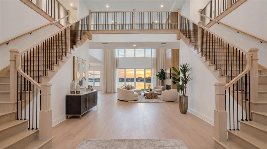 A grand foyer features dual staircases, light wood flooring, and a view of a lake — 9760 LAUREL BERRY DRIVE, ORLANDO, FL