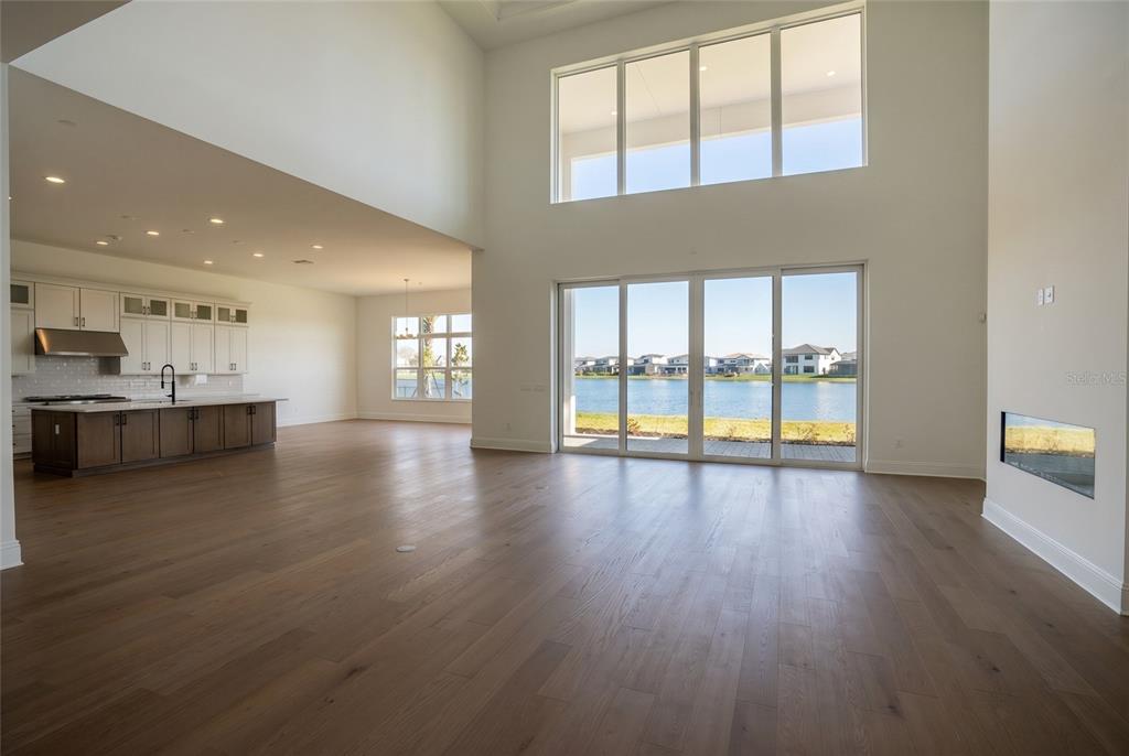 An open-concept living area with high ceilings, hardwood floors, a kitchen, and lake views — 9760 LAUREL BERRY DRIVE, ORLANDO, FL