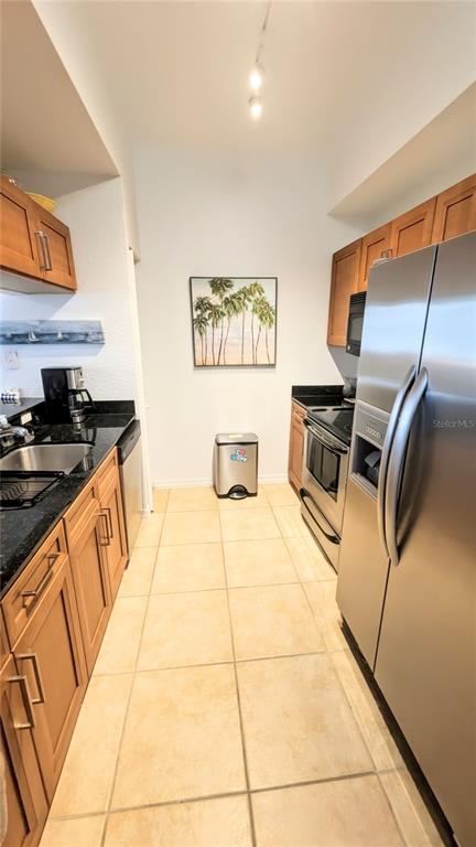 A galley kitchen features wood cabinets, stainless steel appliances, black countertops, and light tile flooring — 1064 N TAMIAMI TRAIL UNIT 1606, SARASOTA, FL