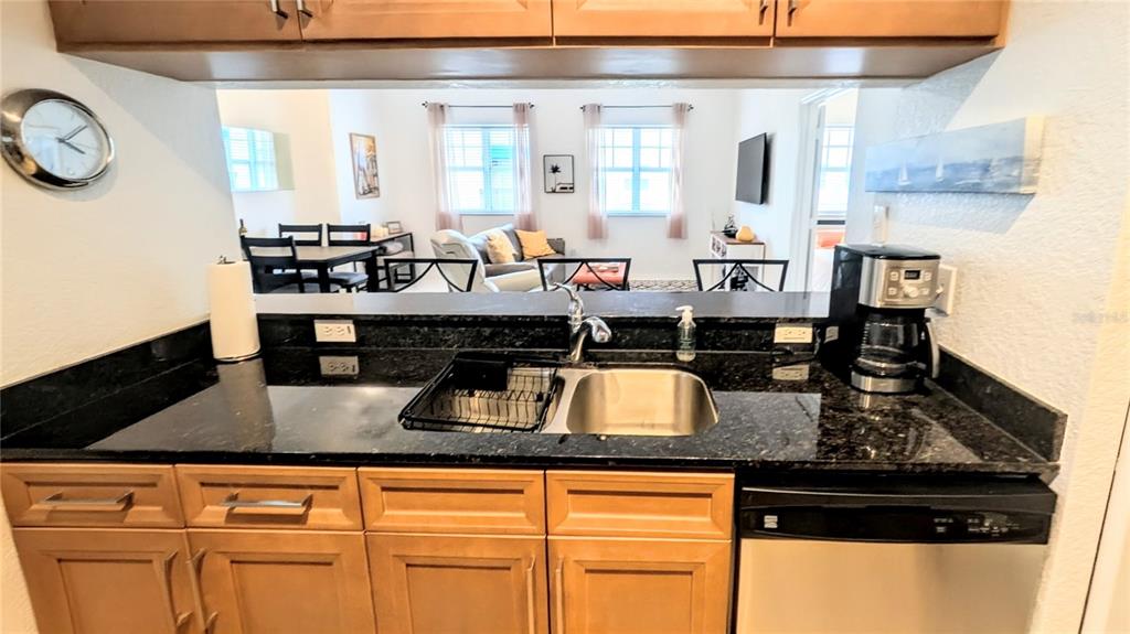 A kitchen with dark granite countertops and light wood cabinets overlooks a living area — 1064 N TAMIAMI TRAIL UNIT 1606, SARASOTA, FL