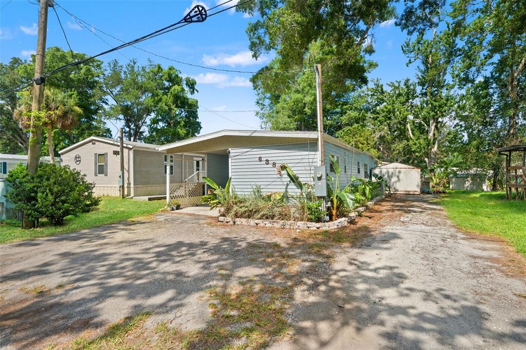 A light blue mobile home with a carport and a gravel driveway under a blue sky — 6380 RICHARD DRIVE, WEEKI WACHEE, FL