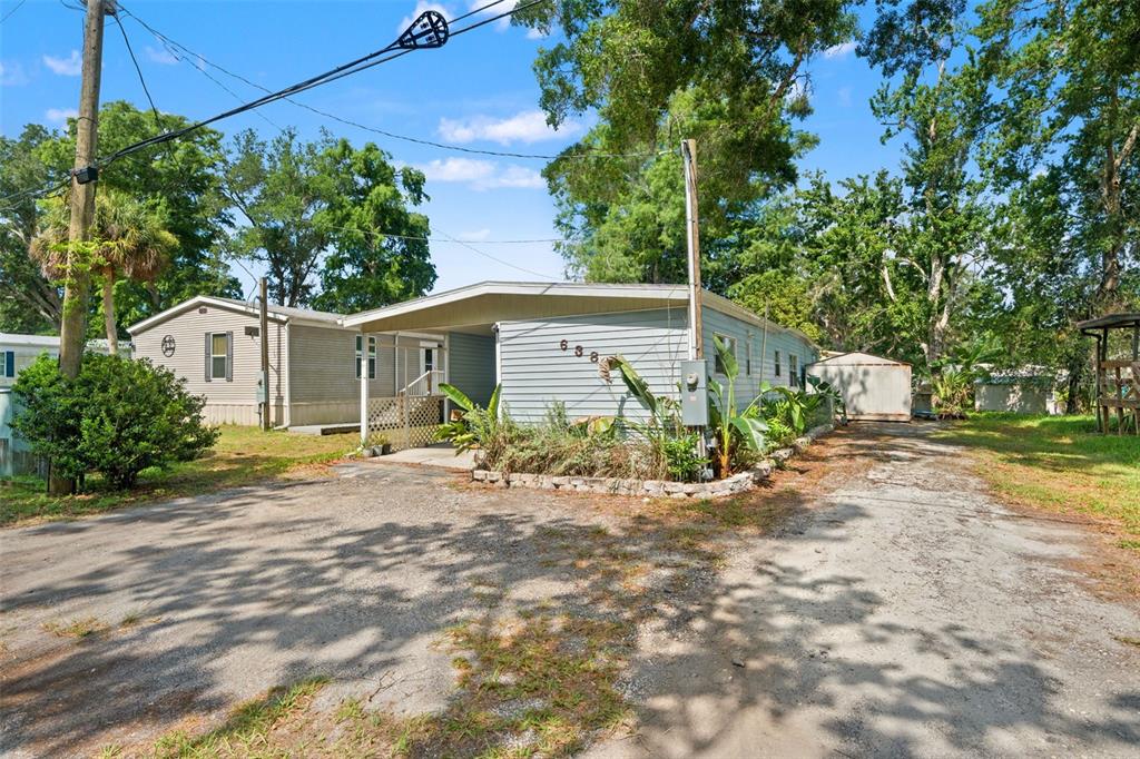 A light blue mobile home with a carport and gravel driveway sits among mature trees — 6380 RICHARD DRIVE, WEEKI WACHEE, FL