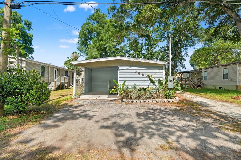 A single-story mobile home with a carport and a gravel driveway under large trees — 6380 RICHARD DRIVE, WEEKI WACHEE, FL