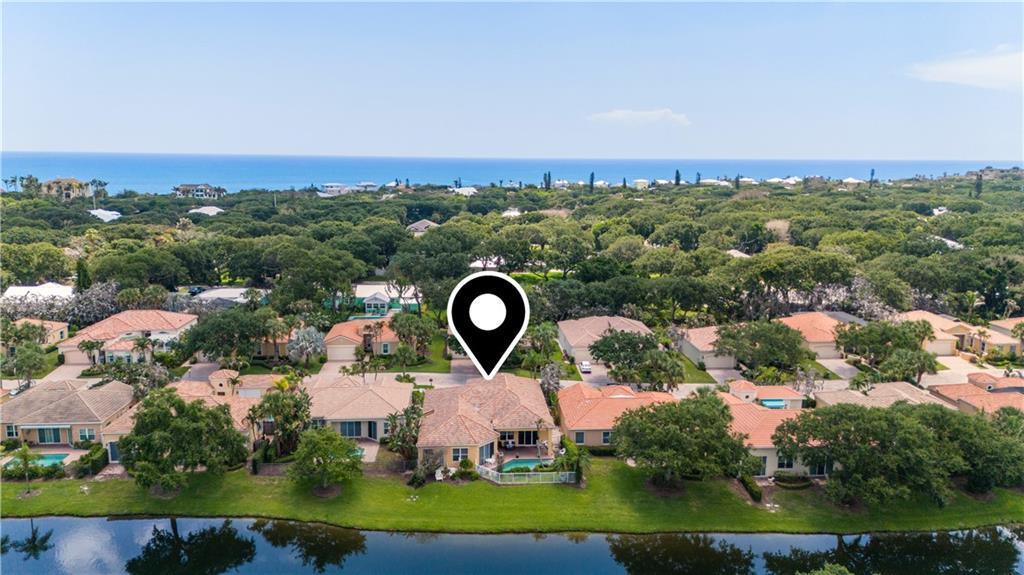 An aerial view shows a residential neighborhood with houses, a lake, and a distant ocean — VERO BEACH, FL