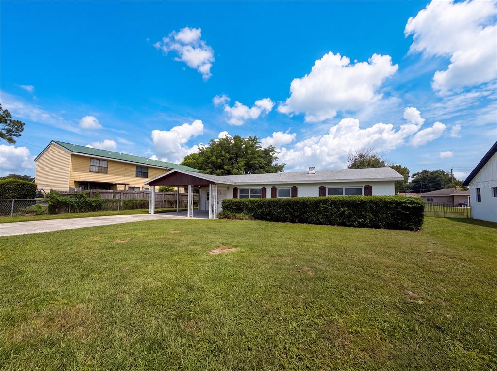 A single-story house with a carport and a large front lawn under a blue sky — 1804 AVENUE Q SW, WINTER HAVEN, FL