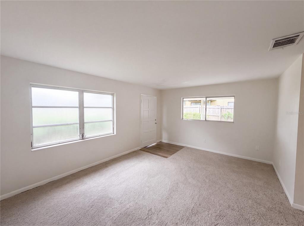 An empty room with beige carpet, white walls, two windows, and a white entry door — 1804 AVENUE Q SW, WINTER HAVEN, FL