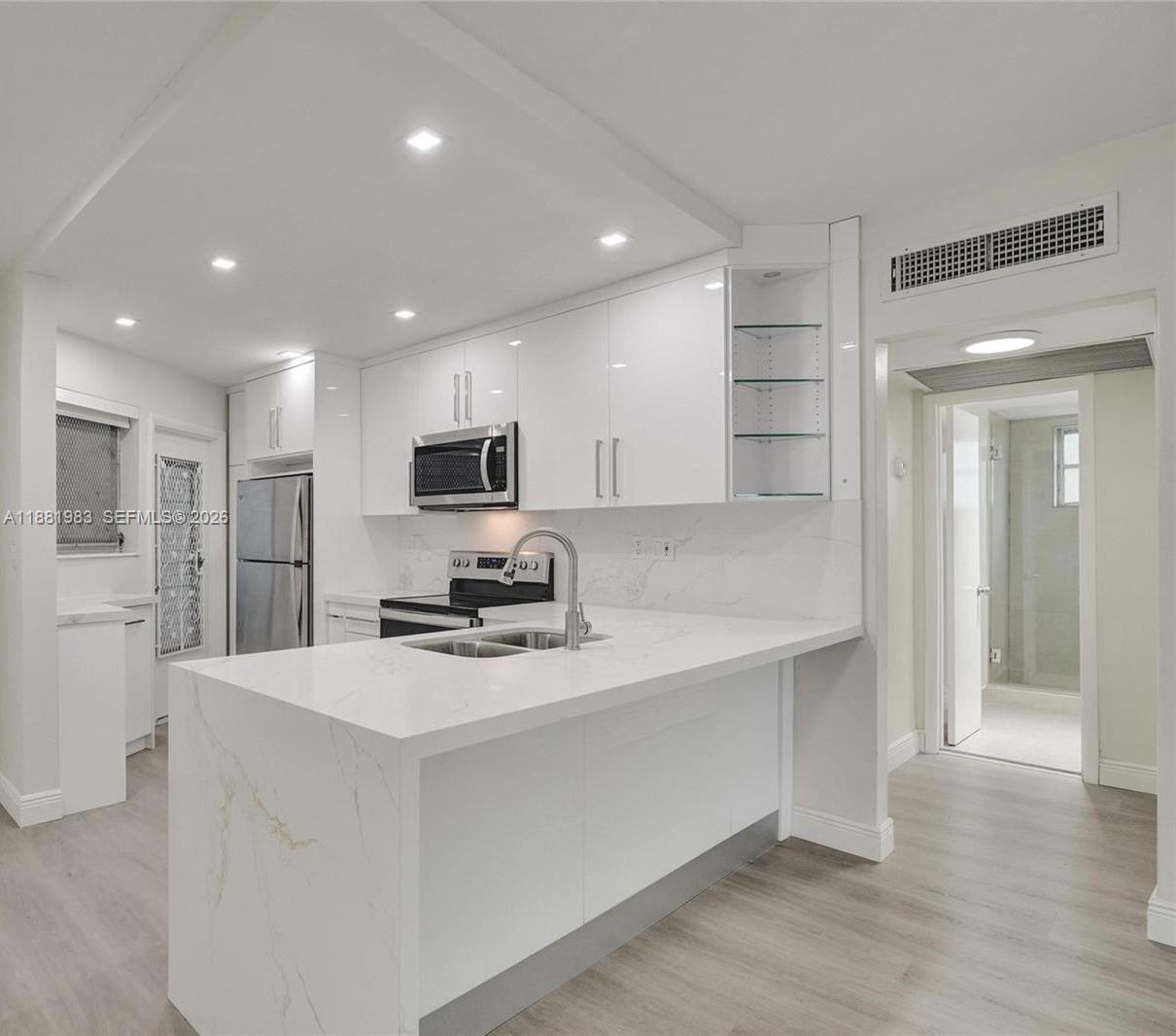 A modern kitchen with white cabinets and a marble-look island opens into a living area — 18720 NE 18th Ave # 116, Miami FL 33179, MIAMI, FL