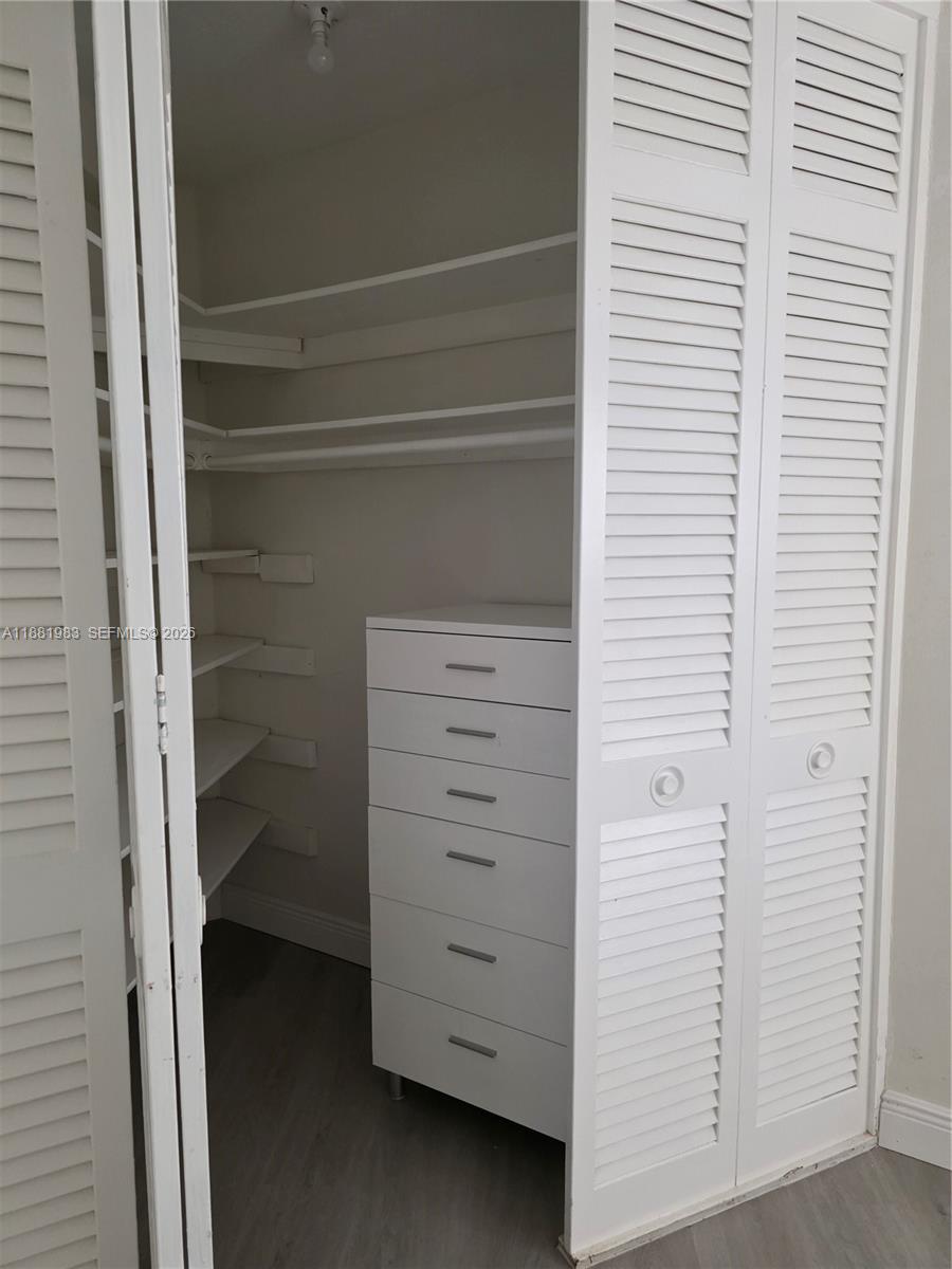 A bedroom features light gray walls, wood-look flooring, a closet, and an attached bathroom — 18720 NE 18th Ave # 116, Miami FL 33179, MIAMI, FL