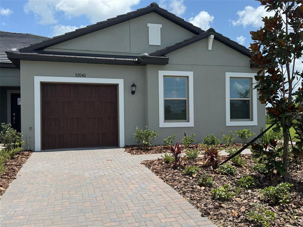 A single-story house with a gray stucco exterior, a brown garage door, and a paver driveway — 32040 GRIFFIN SANDS LN, SAN ANTONIO, FL
