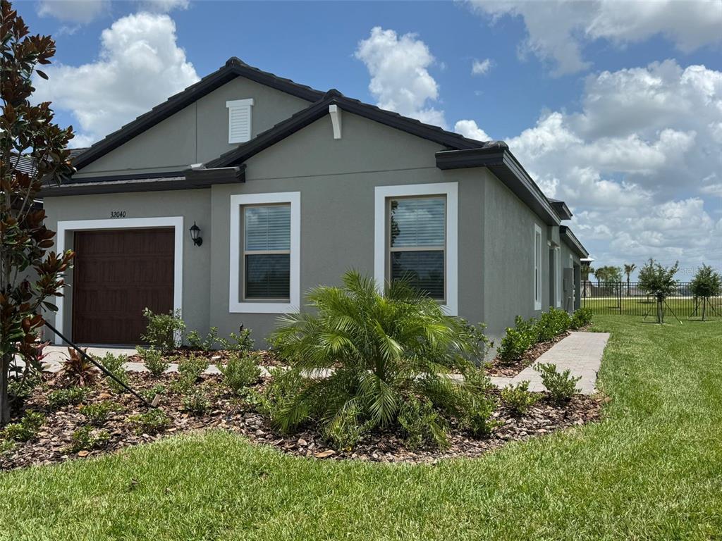 A single-story house with a gray stucco exterior, a brown garage door, and a palm tree — 32040 GRIFFIN SANDS LN, SAN ANTONIO, FL