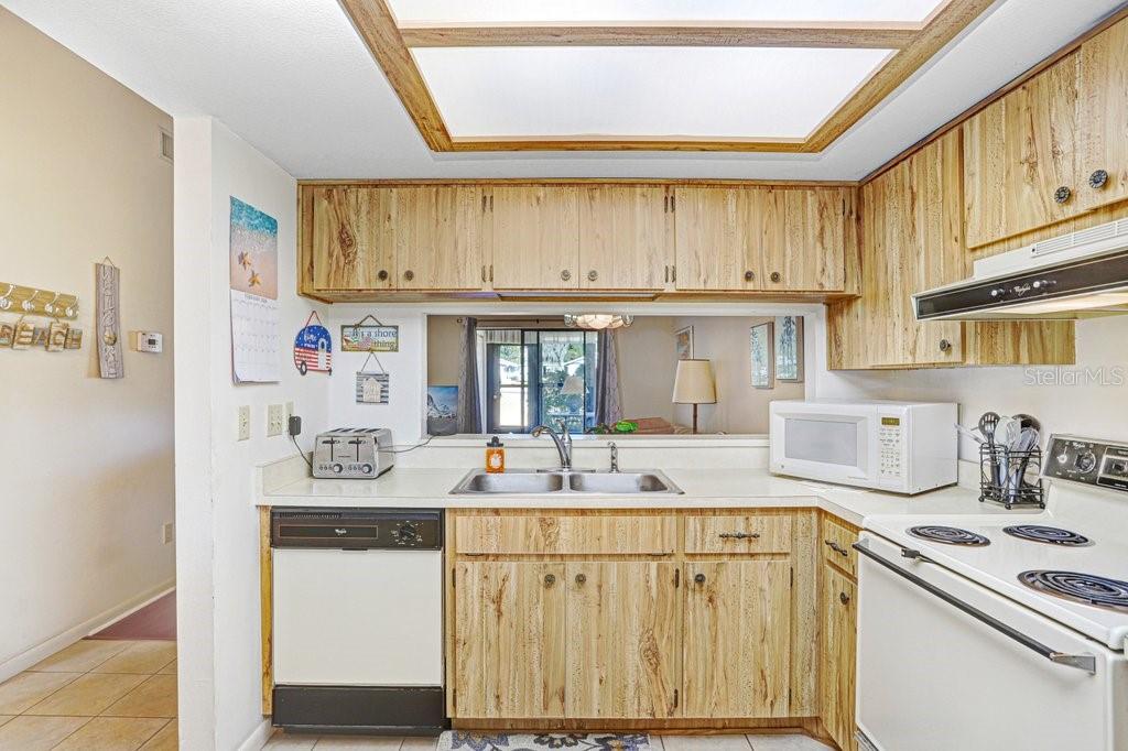 A kitchen features wood-grain cabinets, white countertops, a double sink, and a pass-through window — 38429 COTTONWOOD PLACE, ZEPHYRHILLS, FL