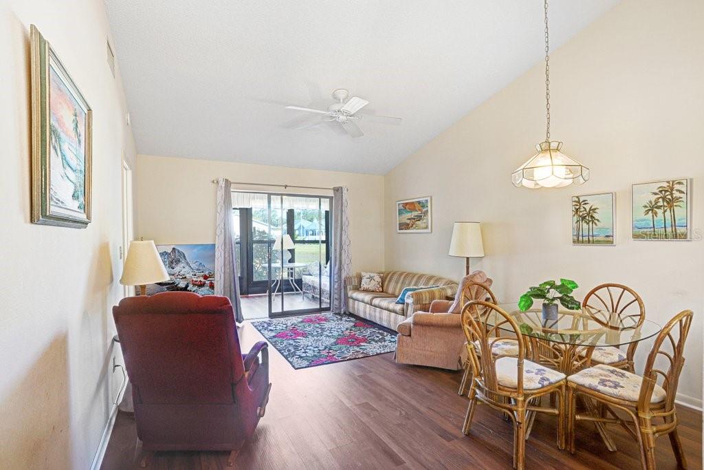 A living and dining area with wood-look flooring, a vaulted ceiling, and sliding glass doors — 38429 COTTONWOOD PLACE, ZEPHYRHILLS, FL