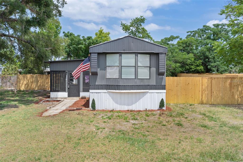 A single-story manufactured home with grey siding, a white skirt, and an American flag — 33514 LUANA COURT, LEESBURG, FL