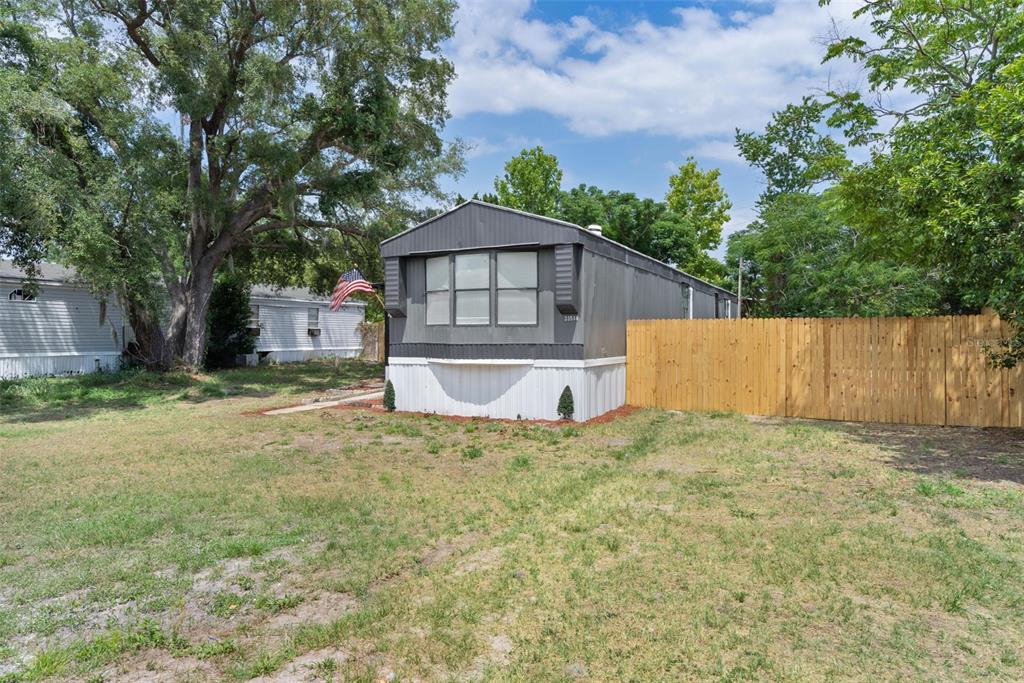 A gray mobile home with a wooden privacy fence sits on a grassy lot — 33514 LUANA COURT, LEESBURG, FL