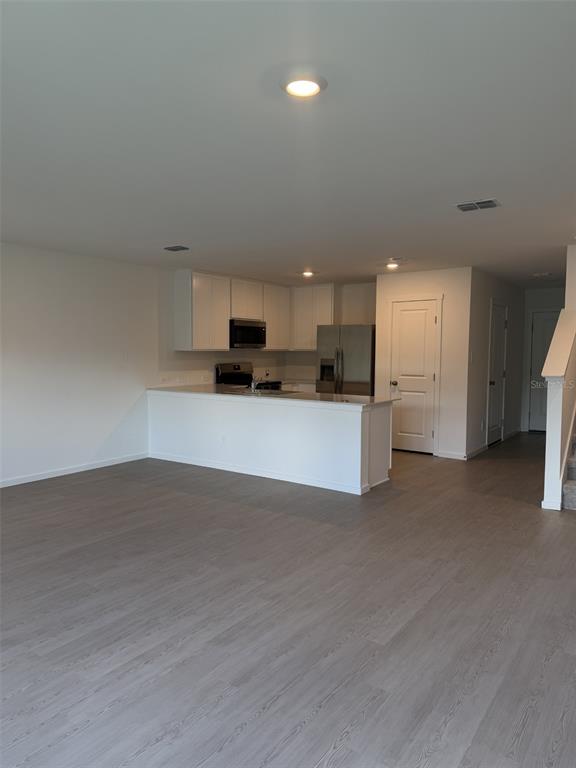 An open-concept kitchen with white cabinets and stainless steel appliances overlooks a living area — 1219 ORION STREET, DAVENPORT, FL